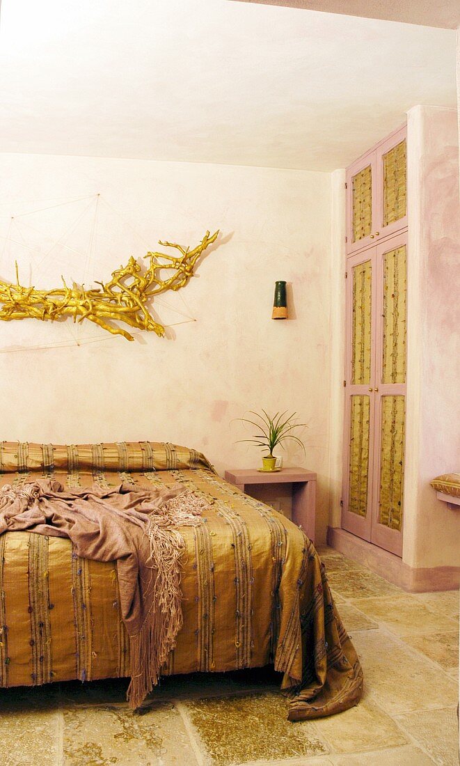 Gold bedspread on double bed below gold hand-crafted artwork in bedroom