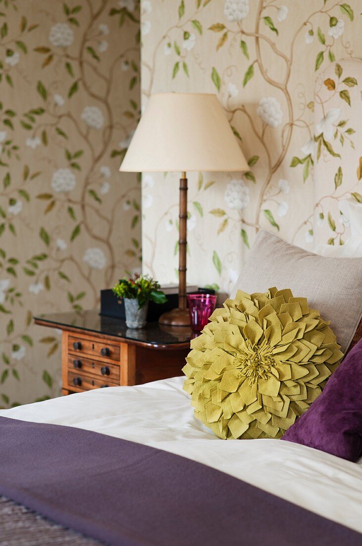 Grünes Blumenkissen auf dem Bett vor Tapete mit floralem Muster