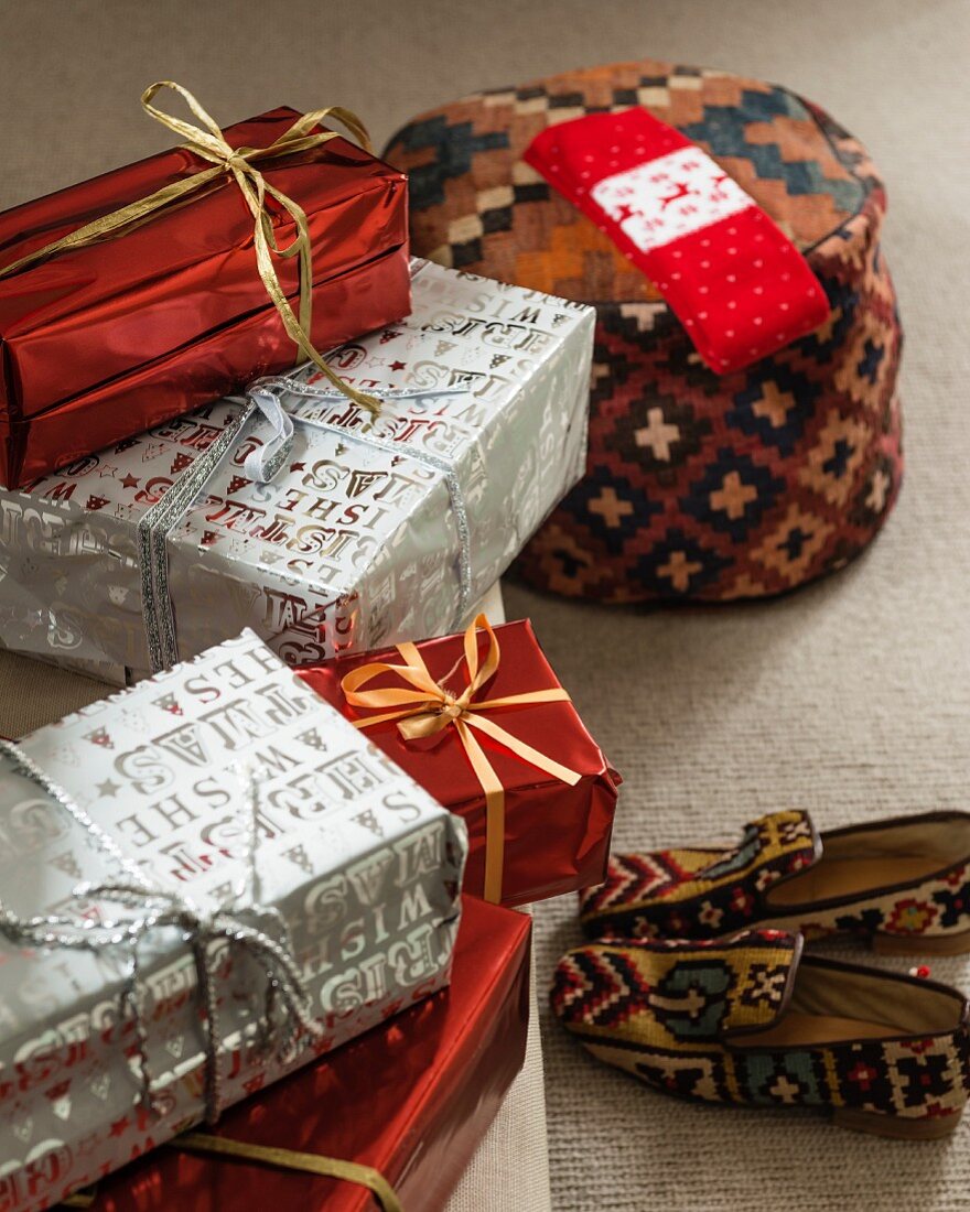 Arrangement mit verpackten Weihnachtsgeschenken, Sitzpouf und Hausschuhen