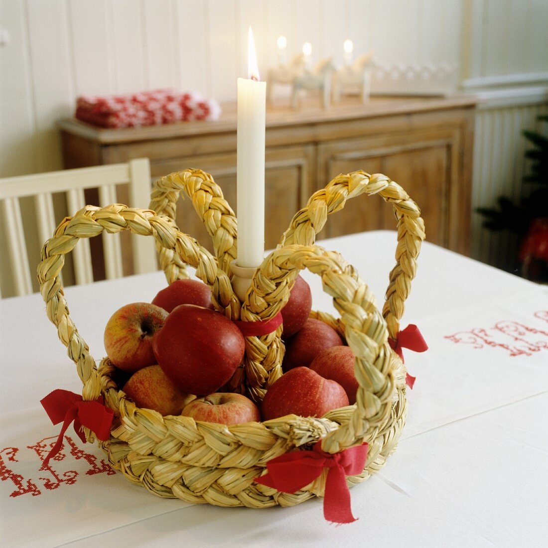 Aus Stroh geflochtene Krone mit Äpfeln und einer Kerze