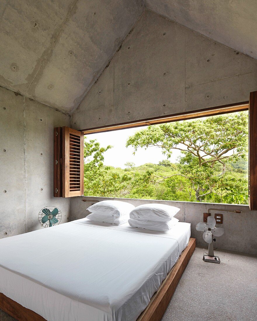 Schlafzimmer aus Holz und Beton mit Panoramafenster in die Natur