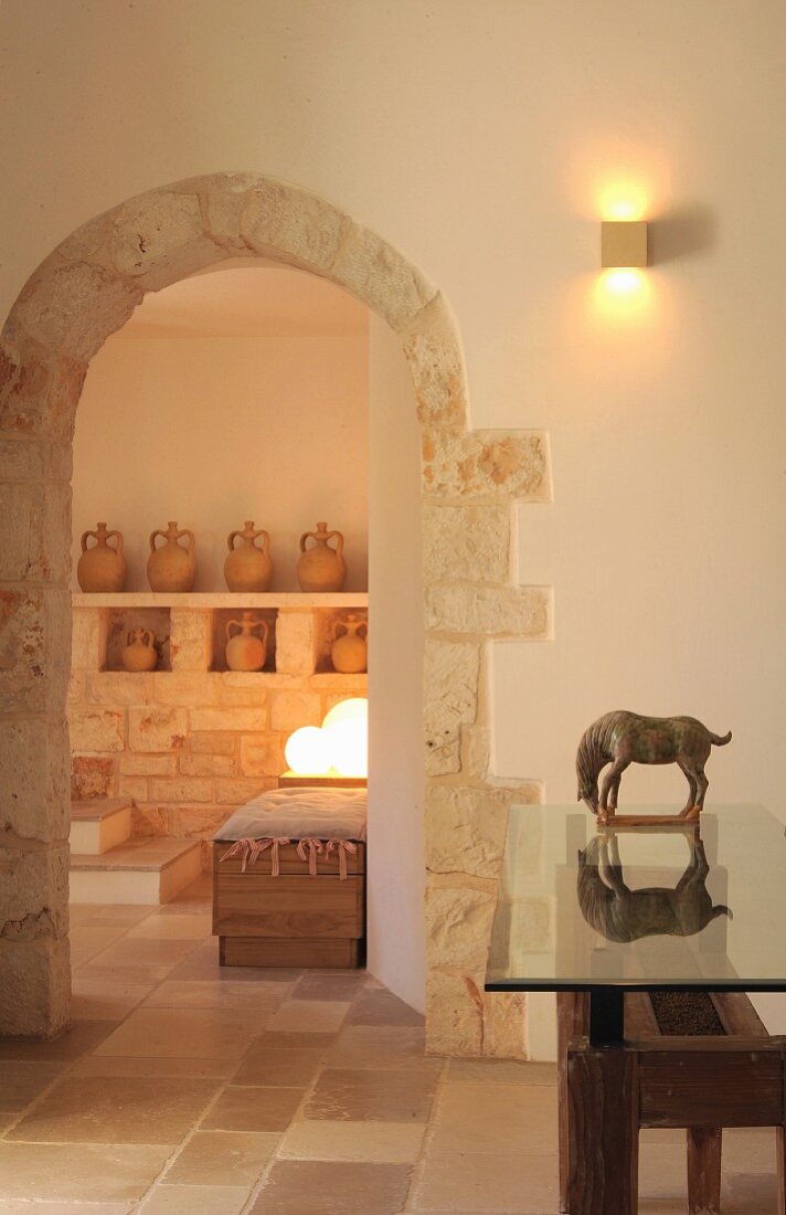 Arched doorways and glass-topped table with wooden base in foyer of trullo
