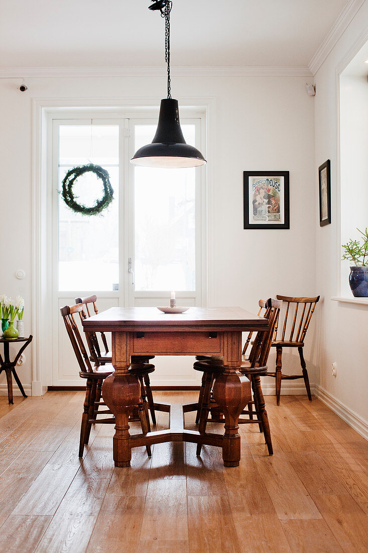 Wooden table with chunky legs and old chairs in bright dining room