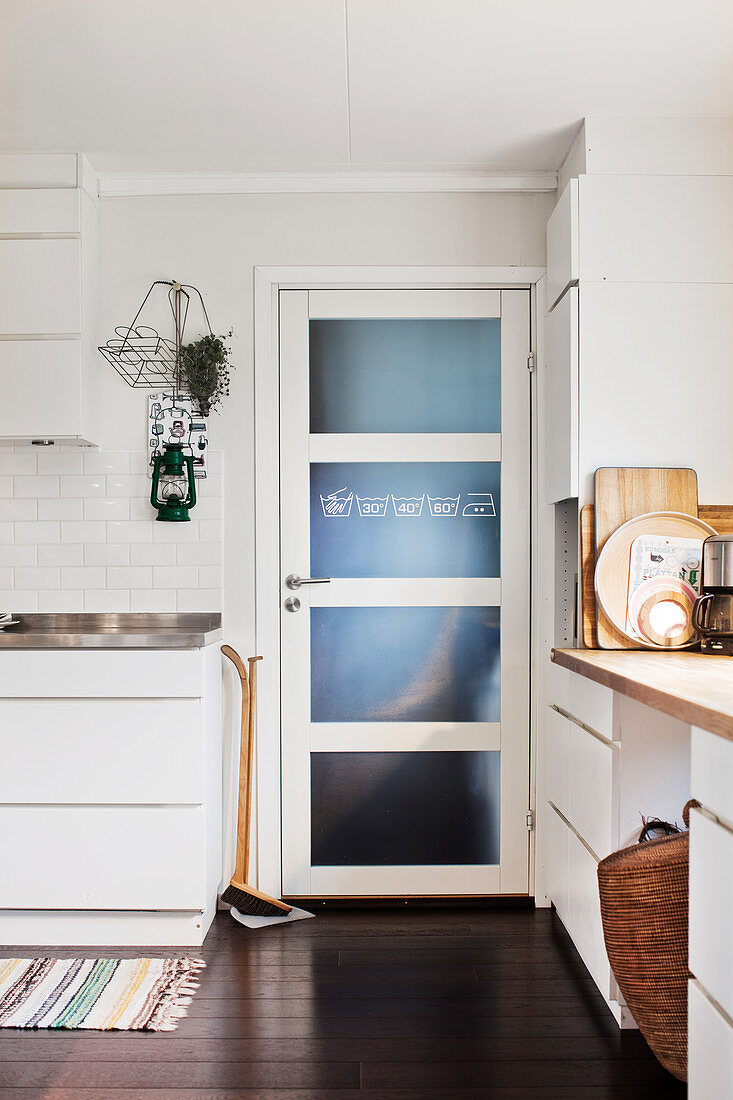 Besen und Schaufel neben Tür mit Glaseinsatz in weißer Küche