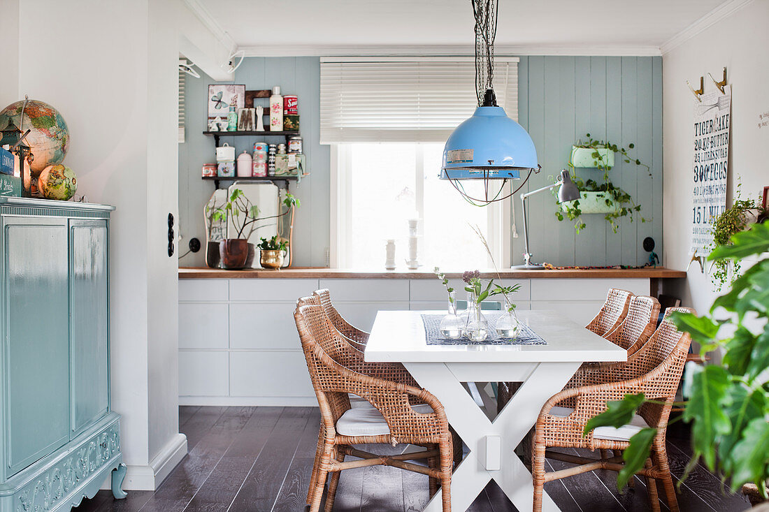 Weißer Esstisch mit Rattanstühlen und hellblau lackierte Kommode mit Türen in offenem Wohnraum