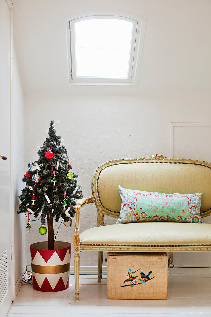 Christmas tree in colourful tub and Baroque couch below skylight