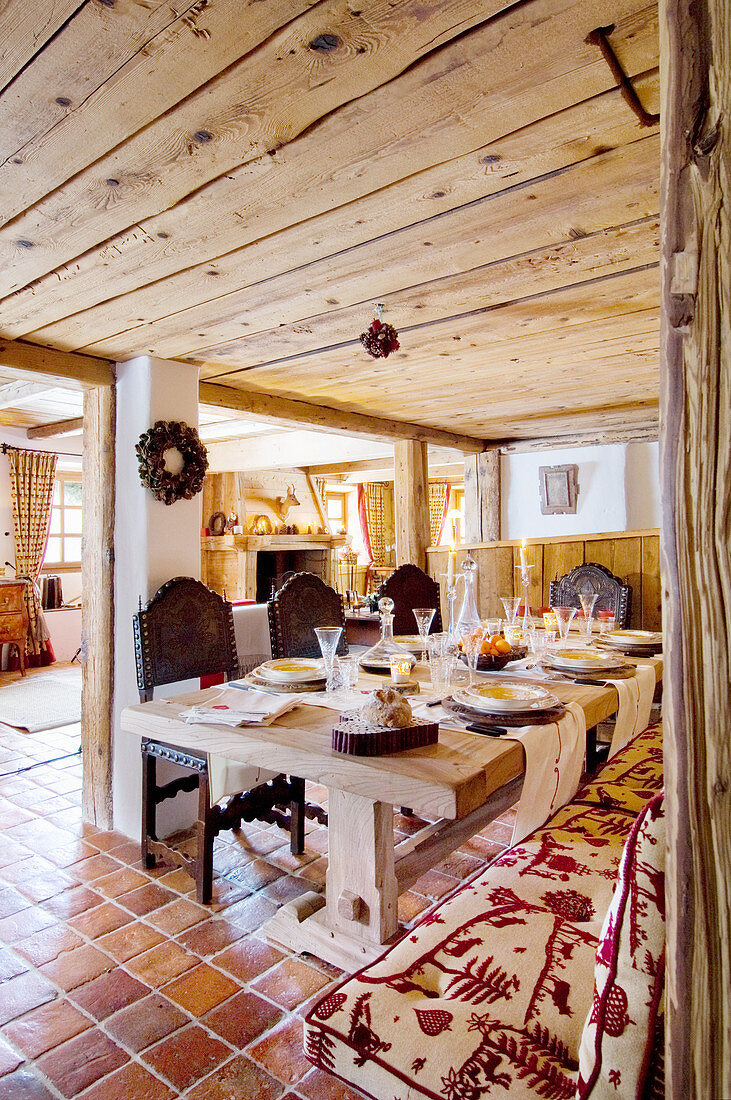 Chunky wooden table and carved wooden chairs on terracotta floor tiles in dining area of chalet