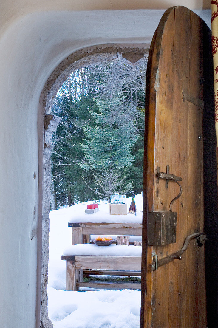 View through rustic, open wooden door to table and benches in snowy landscape
