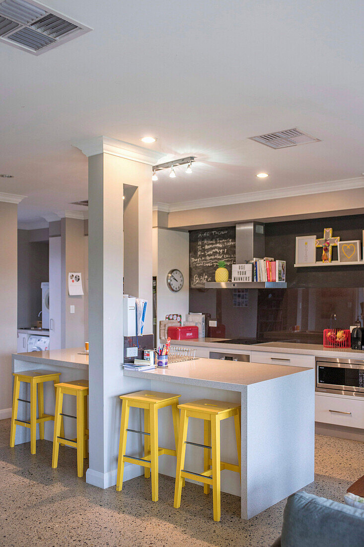 Modern kitchen island with yellow bar stools and blackboard wall in the background