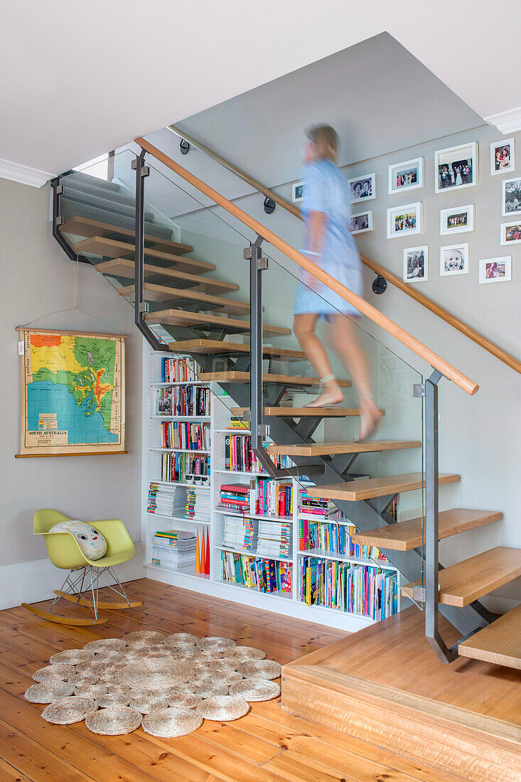 Modern staircase design with glass railing and integrated bookshelf in the living area