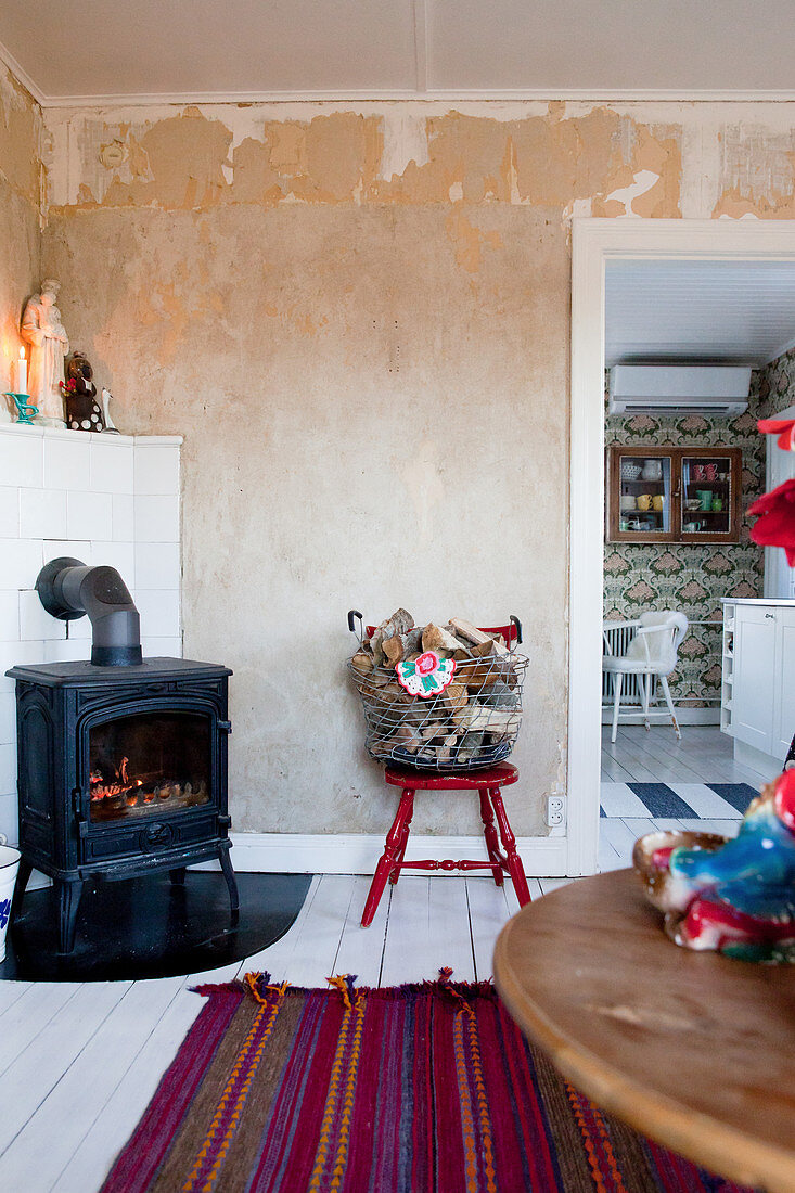 Log burner, basket of firewood on chair and view into kitchen-dining room