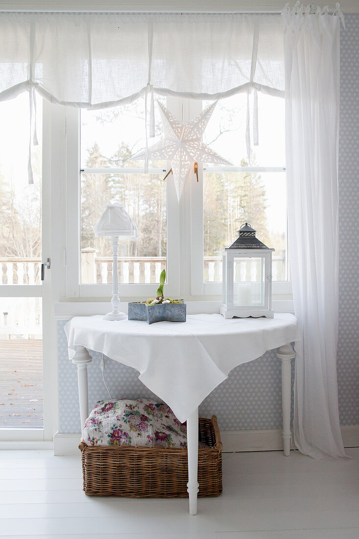 Wintry accessories on console table below window with white curtains