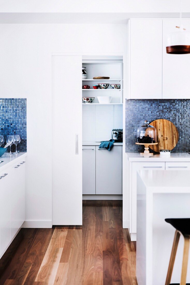weiße Küche mit Holzboden und Schiebetür zur Vorratskammer