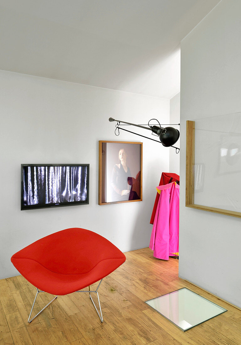 Red designer armchair in front of TV and pictures on wall