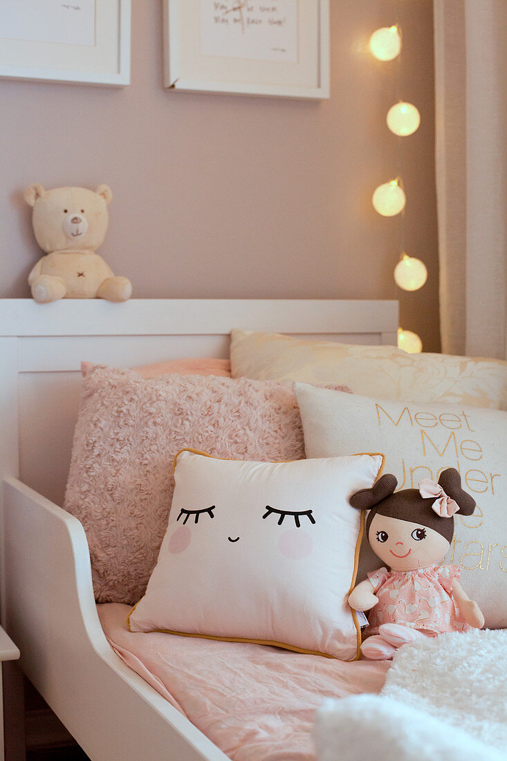 Cushions and doll on child's bed in shades of cream and pink