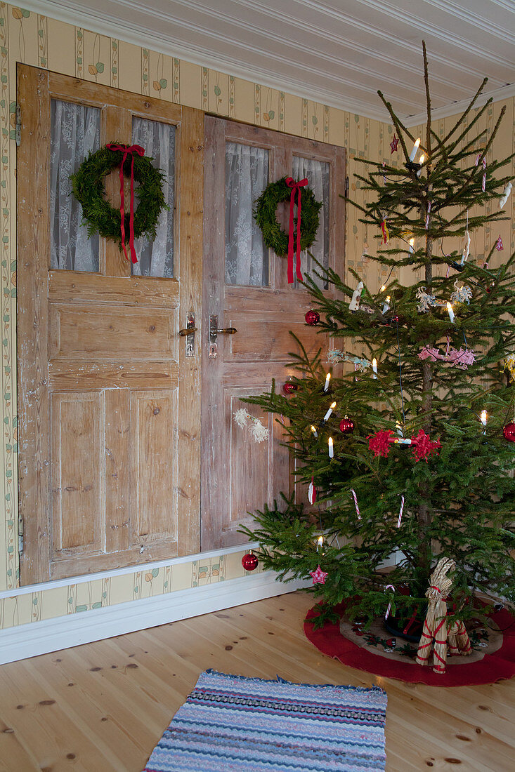 Schlicht dekorierter Weihnachtsbaum vor einem Wandschrank mit zwei Kränzen