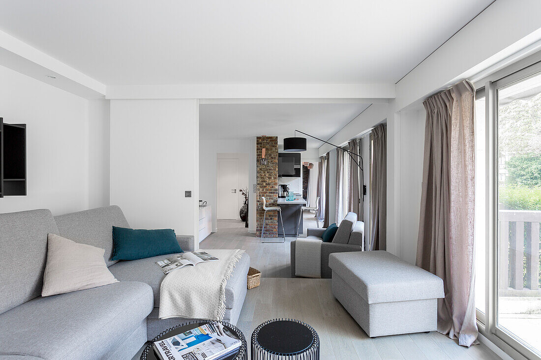 Grey sofa set in bright living room with open sliding door and kitchen in background