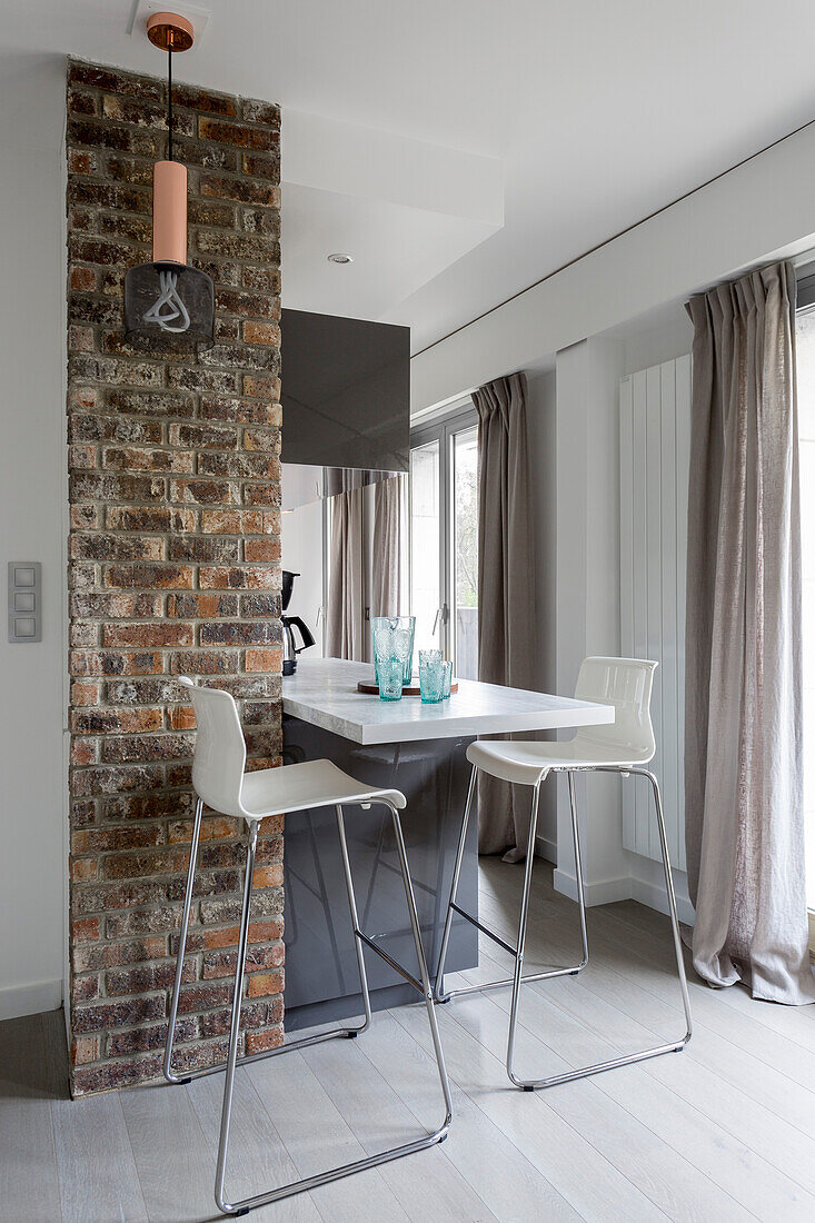 Two modern bar stools at kitchen counter next to brick wall