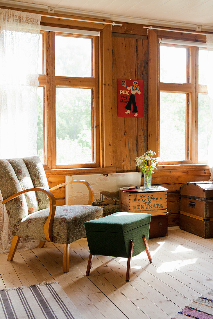 Retro armchair and footstool with storage compartment in front of windows in wooden wall