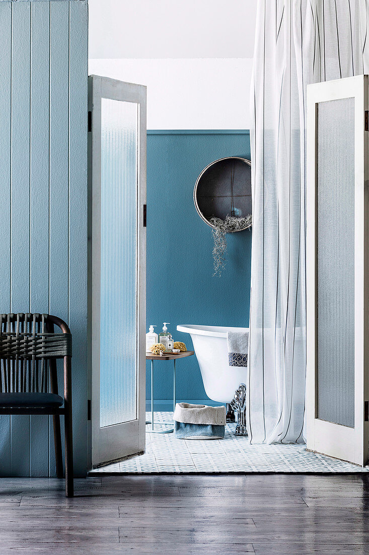 Blick durch geöffnete Saloontüren in blau-weißes Bad eines Strandhauses