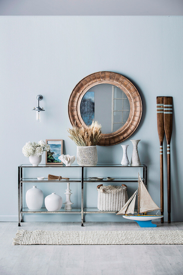 Round wall mirror over a half-high shelf with maritime decorative objects