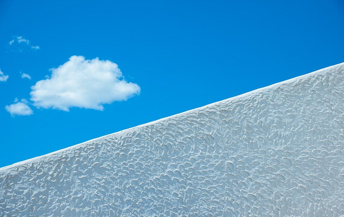 Fluffy cloud in blue sky seen over diagonal white wall