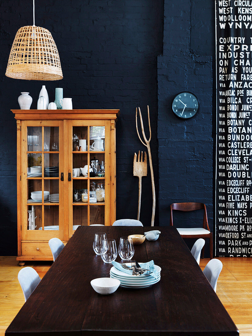 Esstisch mit Stühlen und Vitrinen-Geschirrschrank aus Holz in offenem Wohnraum mit dunkelblauer Wand