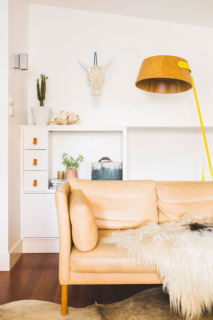 Bright leather couch with fur blanket and floor lamp in front of sideboard