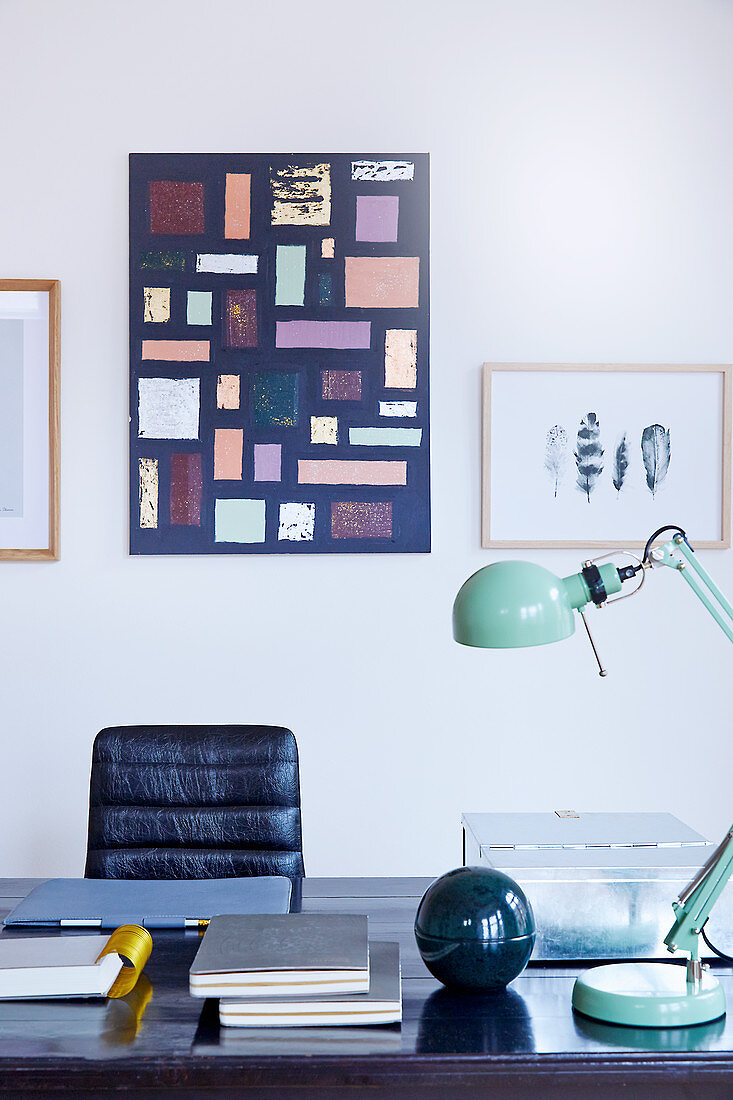 Dunkler Schreibtisch mit mintfarbener Gelenklampe und schwarzem Lederstuhl, Bilder an der Wand