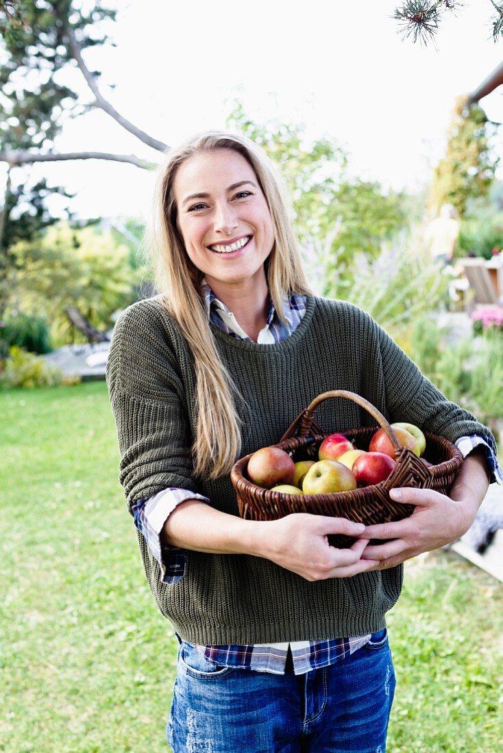 Blonde Frau mit einem Korb frischer Äpfel im Garten