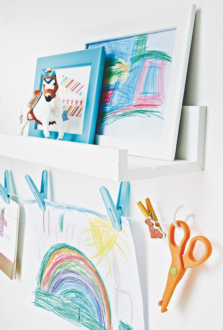A child's drawings on a shelf and hanging on a washing line with pegs in a child's bedroom