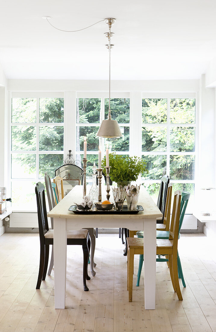 Various brightly coloured chairs around dining table in front of large lattice window