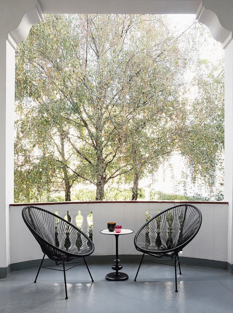 Zwei schwarze Acapulco-Chairs mit Beistelltischchen auf Balkon und Blick auf Bäume