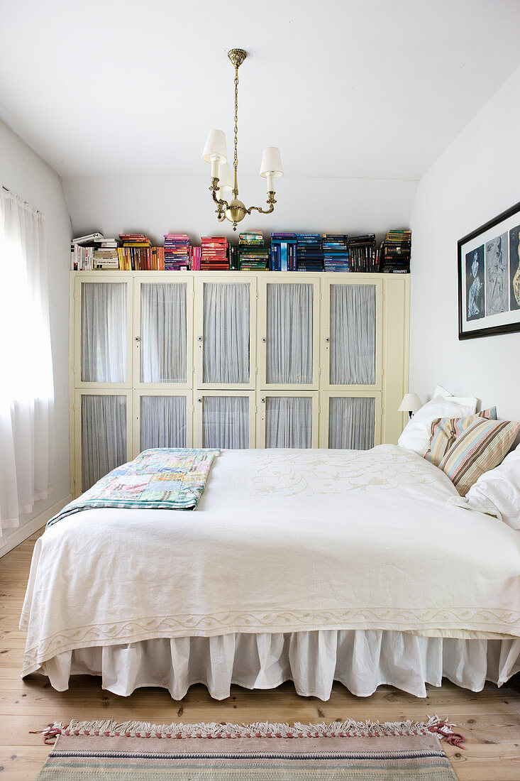 Bed with ruffled valance in front of old fitted wardrobes with glass door panels