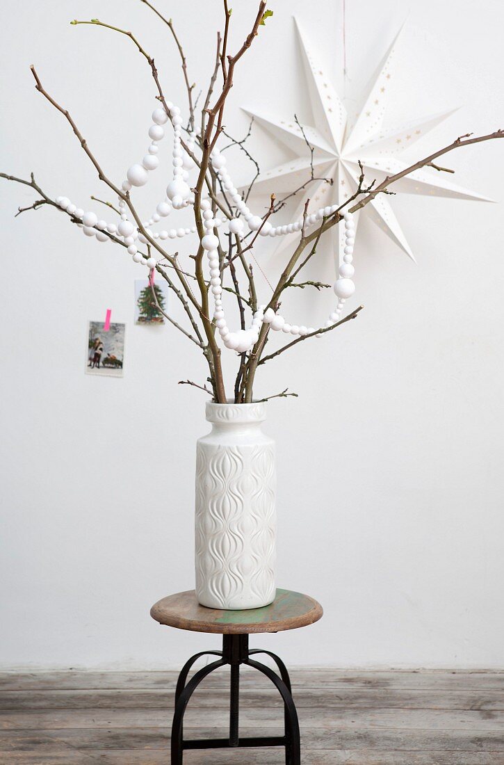 DIY-Girlande aus weißen Papierkugeln um Äste in weißer Vase