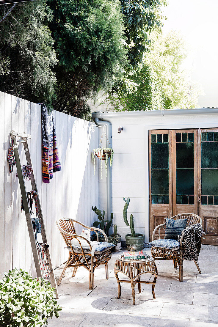 Korbstühle und Holzleiter auf der sonnigen Terrasse im Innenhof