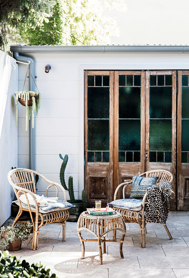 Wicker chairs in front of old glass doors on the sunny courtyard terrace