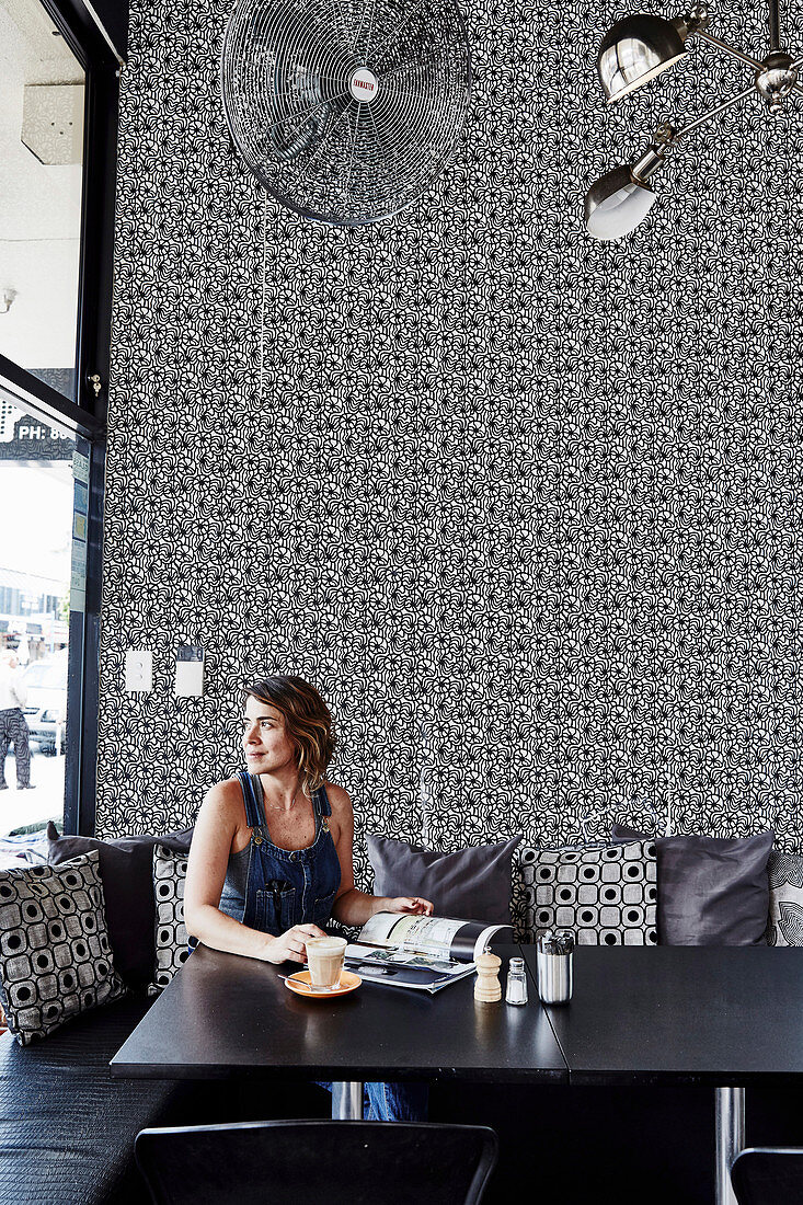 Woman sitting in the restaurant with black and white patterned wallpaper
