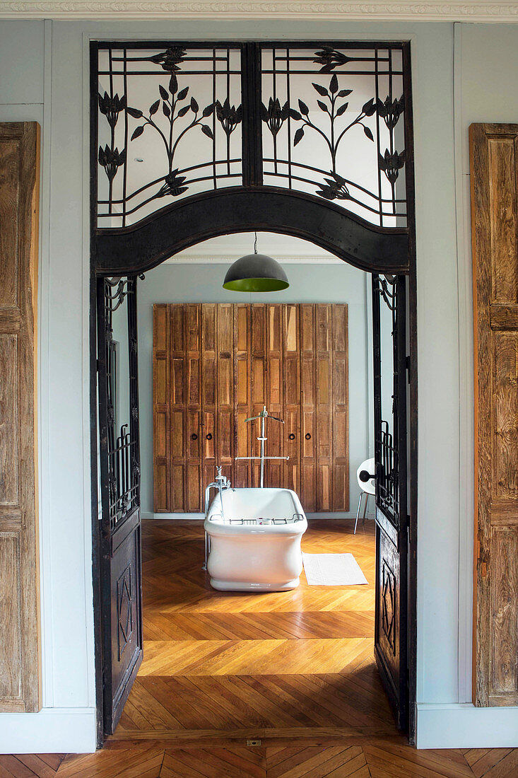 View through wrought iron and glass door into bathroom with free-standing bathtub