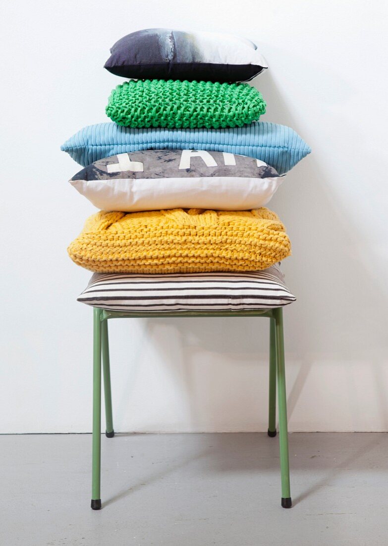 Stacked cushions with hand-made covers on green metal stool