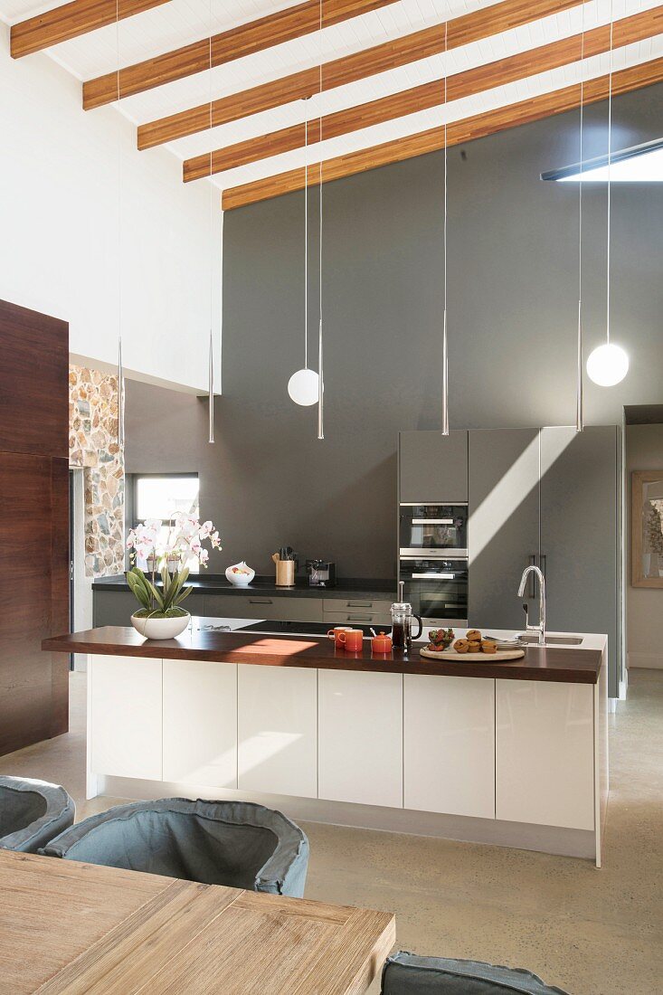 Elegant fitted kitchen with grey back wall and island counter in high-ceilinged room