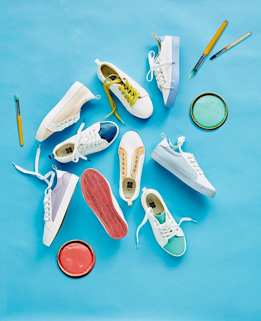 Verschiedene Sneakers, Farbdeckel und Pinsel auf blauem Untergrund