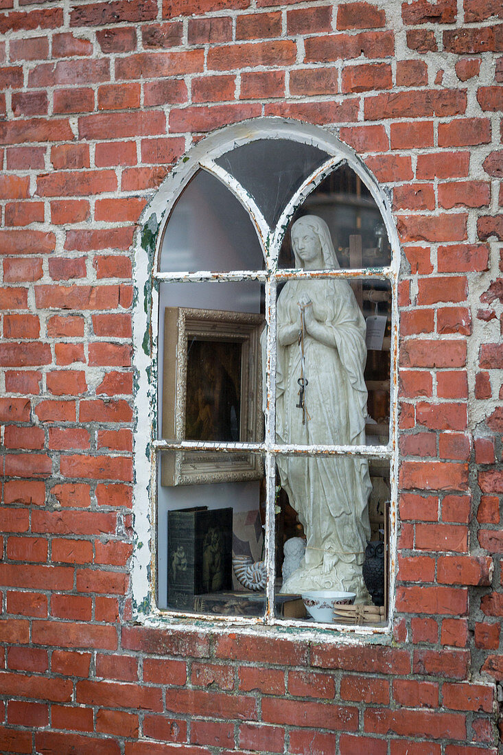 Madonna figurine behind old arched window in brick wall