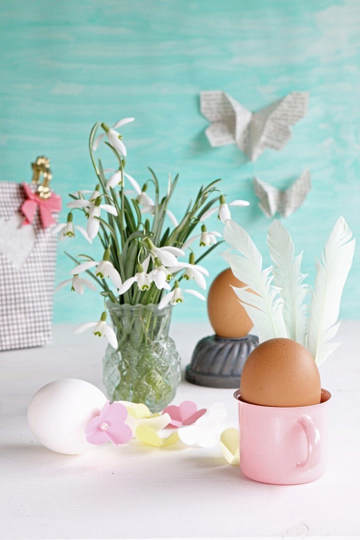 Eggs decorated for Easter with feathers and paper flowers next to vase of snowdrops