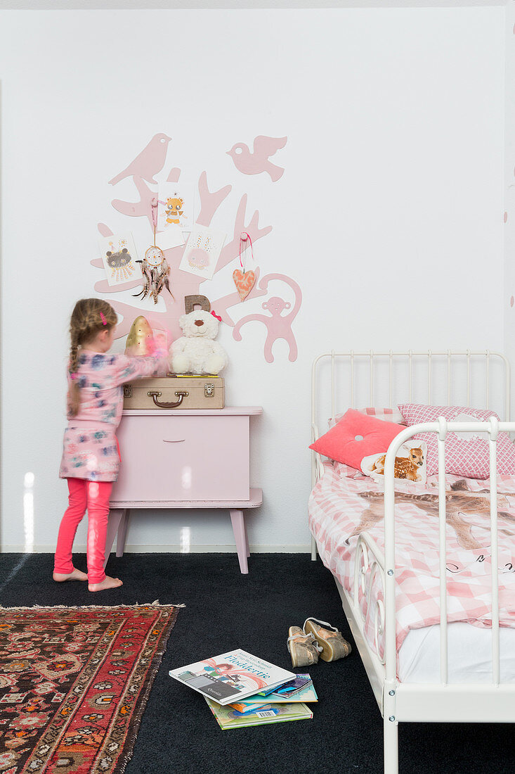 Girl in front of bedside cabinet in child's bedroom with pink accents