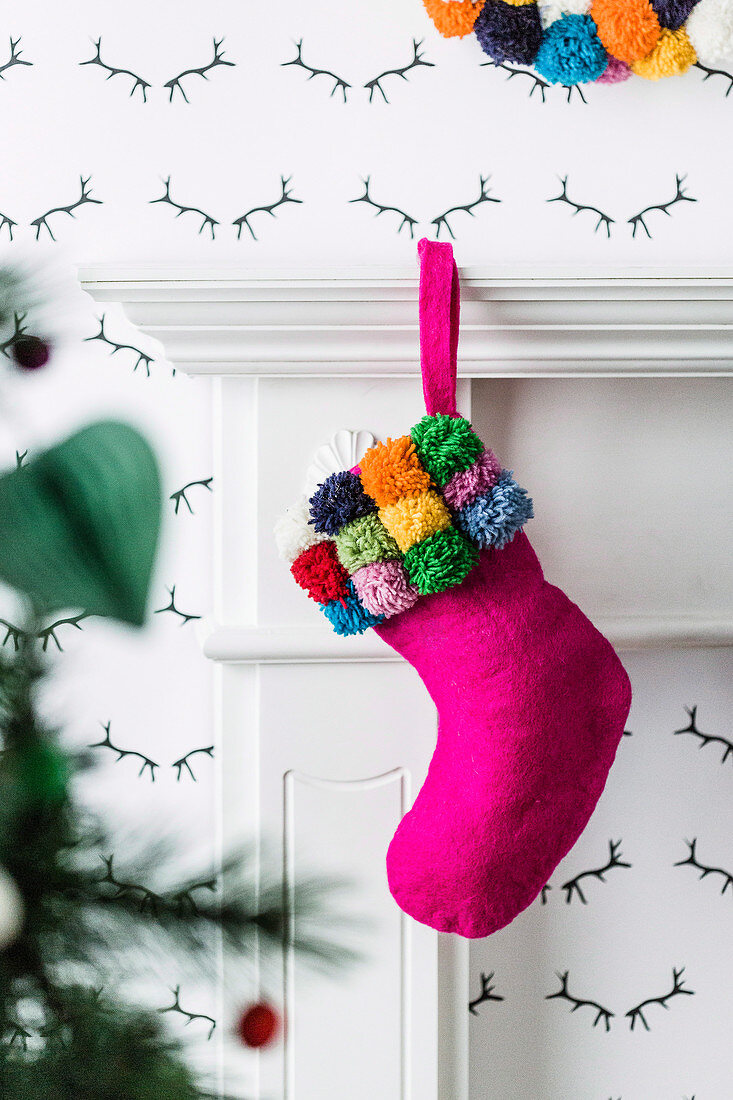 Pink Christmas stocking with pompoms on the fireplace console
