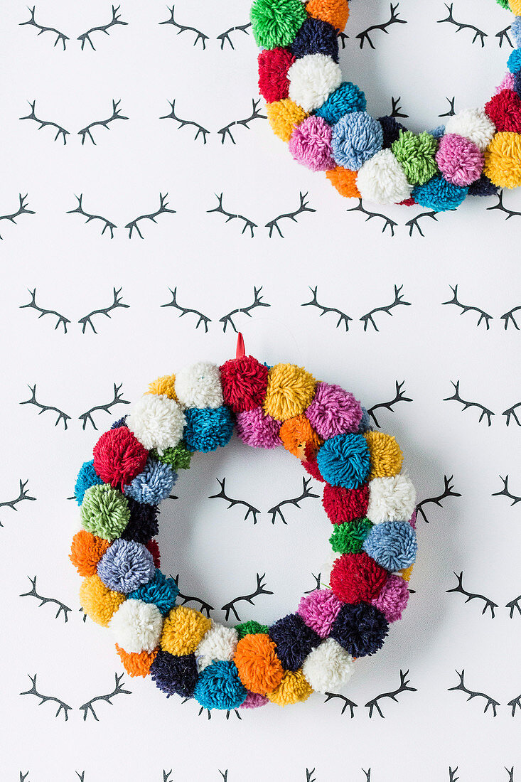 Colorful wreaths of pompoms on the wall with antlers pattern