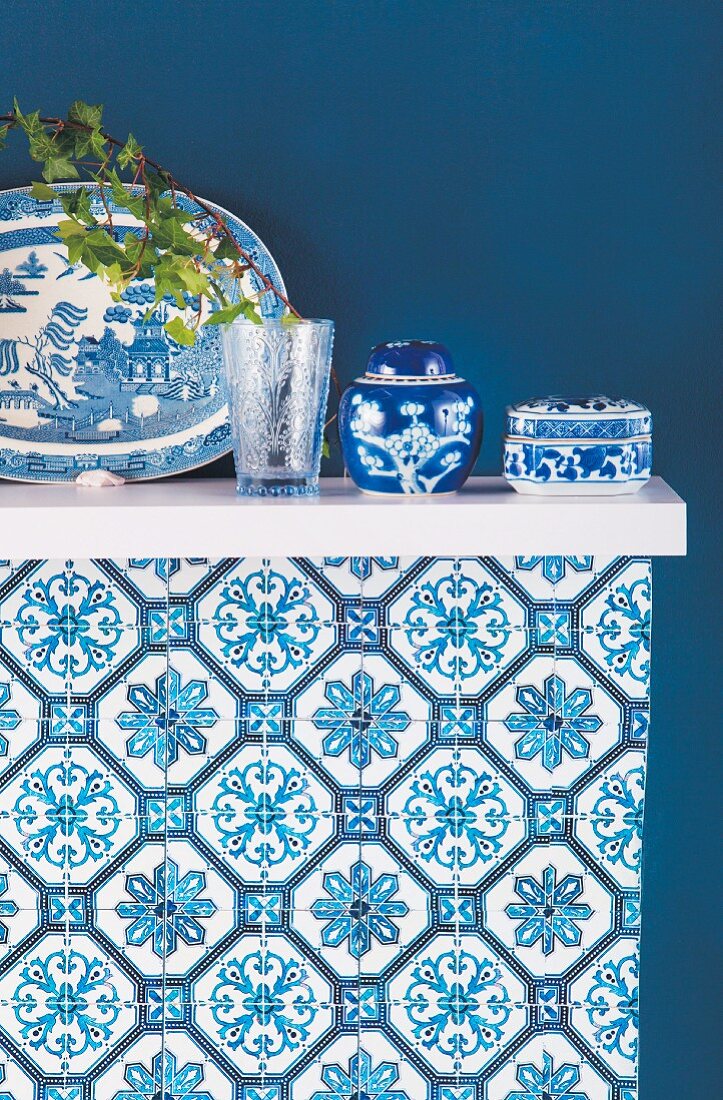 Blau-weißes Asia-Porzellan auf einem Bord vor blauer Wand