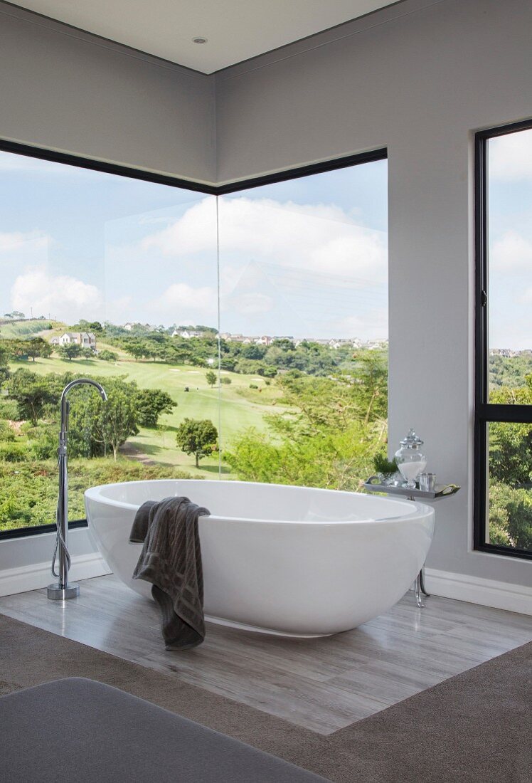 weiße freistehende Badewanne vor Panoramafenster mit Landschaftsblick