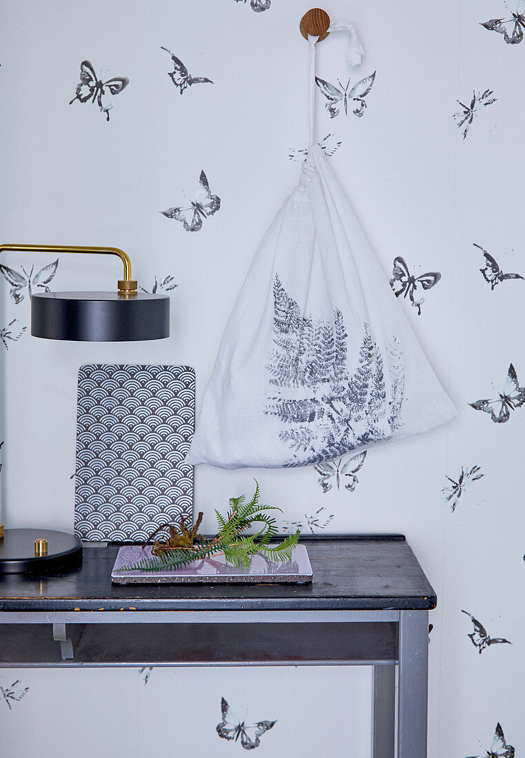 Cloth bag printed with fern leaf hung on wall with butterfly-patterned wallpaper